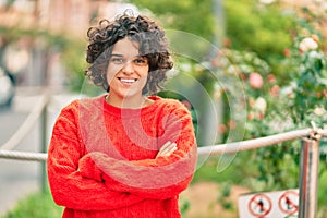 Young hispanic woman with arms crossed smiling happy and looking to the camera at the park