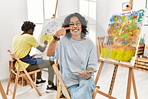 Young hispanic woman at art studio pointing with hand finger to face and nose, smiling cheerful