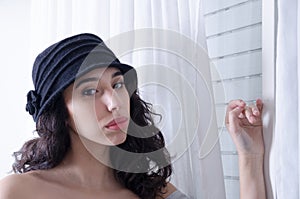 Young hispanic woman with black hat next to a window