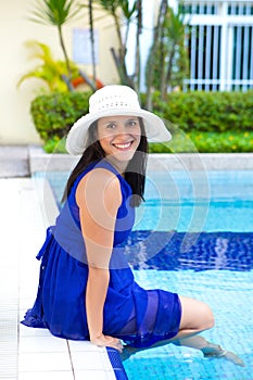 Young hispanic woman in blue dress relaxing by the swimming pool