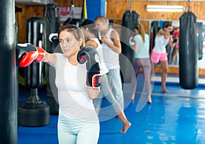 Young hispanic woman in boxing gloves practicing punches on punchbag