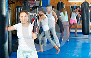 Young hispanic woman in boxing gloves practicing punches on punchbag