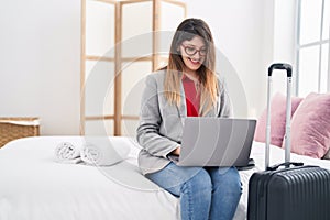 Young hispanic woman business worker using laptop sitting on bed at hotel room