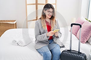 Young hispanic woman business worker using smartphone sitting on bed at hotel room