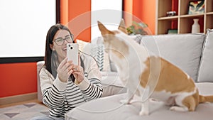 Young hispanic woman with chihuahua dog sitting on the floor taking photo with smartphone at home