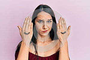 Young hispanic woman covering eyes with hands and fake lashes skeptic and nervous, frowning upset because of problem