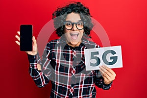 Young hispanic woman with curly hair holding 5g technology smartphone celebrating crazy and amazed for success with open eyes