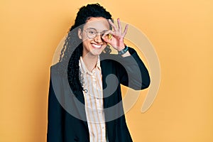 Young hispanic woman with curly hair wearing business clothes smiling happy doing ok sign with hand on eye looking through fingers