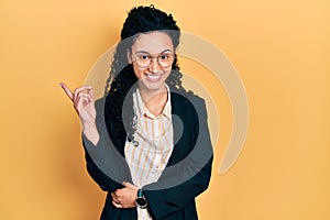 Young hispanic woman with curly hair wearing business clothes smiling happy pointing with hand and finger to the side