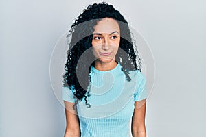 Young hispanic woman with curly hair wearing casual blue t shirt smiling looking to the side and staring away thinking