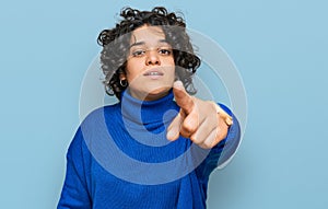 Young hispanic woman with curly hair wearing turtleneck sweater pointing displeased and frustrated to the camera, angry and