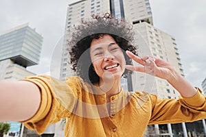Young hispanic woman with curly hair, yellow shirt and cheerful attitude, smiling and having fun taking a selfie photo