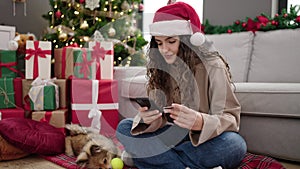 Young hispanic woman with dog shopping with smartphone and credit card celebrating christmas at home