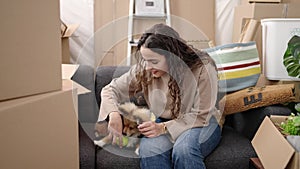 Young hispanic woman with dog sitting on sofa playing with ball at new home