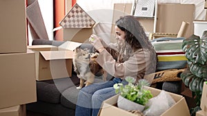 Young hispanic woman with dog sitting on sofa playing with ball at new home