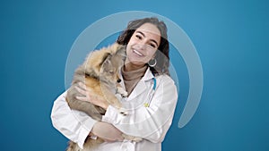 Young hispanic woman with dog veterinarian smiling confident hugging over isolated blue background