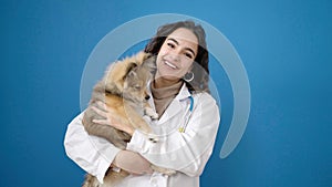 Young hispanic woman with dog veterinarian smiling confident hugging over isolated blue background