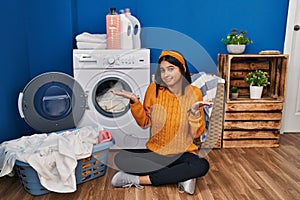 Young hispanic woman doing laundry clueless and confused expression with arms and hands raised