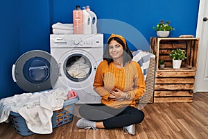 Young hispanic woman doing laundry with hand on stomach because indigestion, painful illness feeling unwell