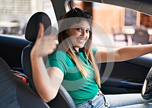 Young hispanic woman doing ok gesture driving car at street
