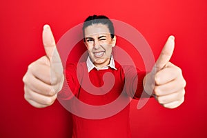 Young hispanic woman doing thumbs up positive gesture winking looking at the camera with sexy expression, cheerful and happy face