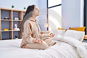 Young hispanic woman doing yoga exercise sitting on bed at bedroom