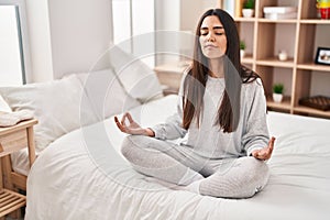 Young hispanic woman doing yoga exercise sitting on bed at bedroom