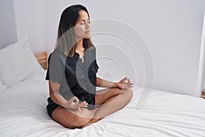 Young hispanic woman doing yoga exercise sitting on bed at bedroom