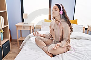 Young hispanic woman doing yoga exercise sitting on bed at bedroom