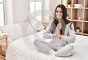 Young hispanic woman doing yoga exercise sitting on bed at bedroom