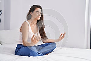 Young hispanic woman doing yoga exercise sitting on bed at bedroom