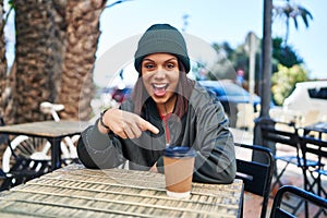 Young hispanic woman drinking a cup of coffee outdoors smiling happy pointing with hand and finger