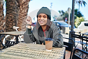 Young hispanic woman drinking a cup of coffee outdoors smiling happy pointing with hand and finger to the side