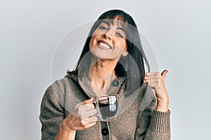 Young hispanic woman drinking a cup of coffee pointing thumb up to the side smiling happy with open mouth