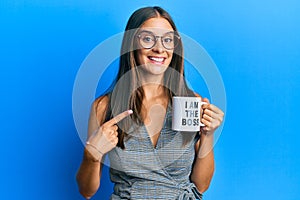 Young hispanic woman drinking from i am the boss coffee cup smiling happy pointing with hand and finger