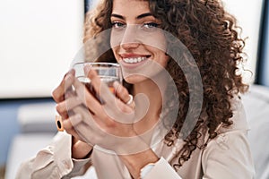 Young hispanic woman drinking tea sitting on sofa at home