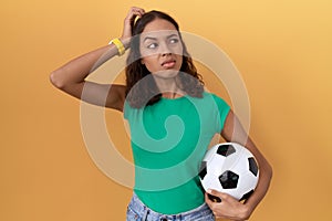 Young hispanic woman holding ball confuse and wondering about question