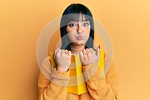 Young hispanic woman holding book puffing cheeks with funny face