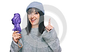 Young hispanic woman holding closed purple umbrella surprised with an idea or question pointing finger with happy face, number one