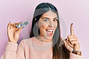 Young hispanic woman holding computer memory smiling with an idea or question pointing finger with happy face, number one