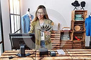 Young hispanic woman holding dollars working at clothing store