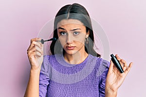 Young hispanic woman holding eyelashes curler skeptic and nervous, frowning upset because of problem