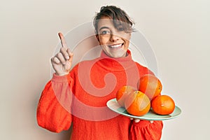 Young hispanic woman holding fresh oranges surprised with an idea or question pointing finger with happy face, number one