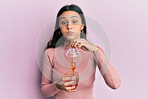 Young hispanic woman holding honey puffing cheeks with funny face