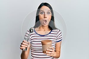 Young hispanic woman holding ice cream afraid and shocked with surprise and amazed expression, fear and excited face