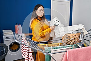 Young hispanic woman holding magnifying glass looking for stain at clothes looking at the camera blowing a kiss being lovely and