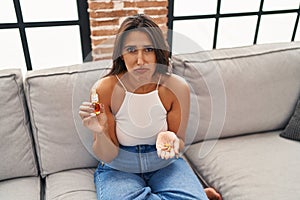 Young hispanic woman holding pills and cbd oil depressed and worry for distress, crying angry and afraid