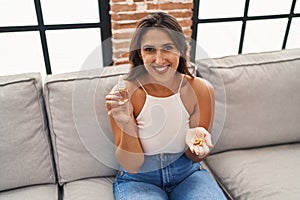 Young hispanic woman holding pills and cbd oil smiling with a happy and cool smile on face