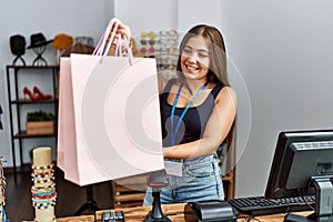 Young hispanic woman holding shopping bag working at clothing store