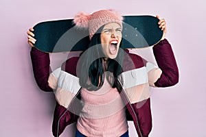 Young hispanic woman holding skate angry and mad screaming frustrated and furious, shouting with anger